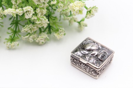 Caixa de comprimidos em prata com altos relevos e rosa relevada na tampa